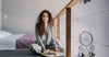 Woman in silk pyjamas reading book by bed in cosy winter evening — July slow evening rituals silk Calliope Studio Australia