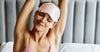 Woman in silk sleepwear stretching with sleep mask on in the morning — winter self-care skin and sleep routine Calliope Studio